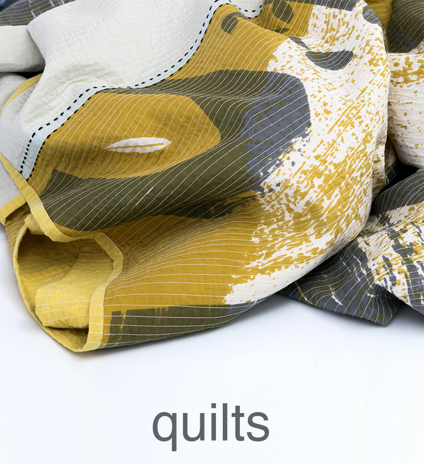 Close-up of a quilt with abstract patterns in yellow, gray, and white.