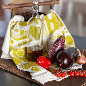 Glass bottle with a wooden board containing a printed tea towel called Veggie.