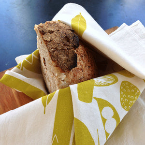 Tea-towel handprinted design called Veggie wrapping a hunk of bread on a board.