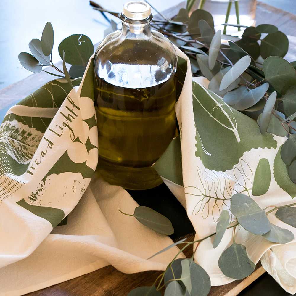 Clear glass bottle with olive oil on a handprinted tea towel called Leaves