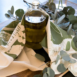 Clear glass bottle with olive oil on a handprinted tea towel called Leaves