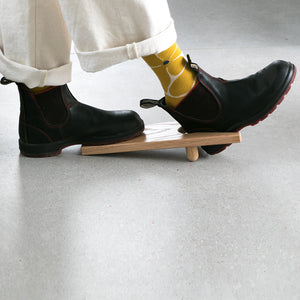 Person wearing black boots  using oak wood boot jack.