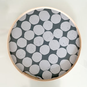 A round, Gray-on-gray printed dot tray. Hand-printed design featuring PilgrimWaters dots on a dark gray white background, with a natural ash wood edge. The tray is displayed head-on