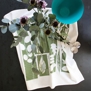 Leaves tea towel by PilgrimWaters — overhead lifestyle shot with plant leaves and a bowl on a dark tabletop