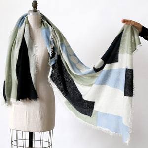 Totem George scarf draped over a mannequin and held by a hand against a white background. Design by PilgrimWaters. Printed in Nepal. Copyright 2026 Susy Pilgrimaters. 