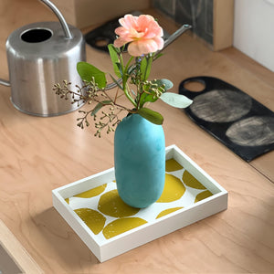 PilgrimWaters Ochre colorway handcrafted Mini-Mini tray featuring a bold graphic dot pattern, styled on a wooden tabletop with a turquoise ceramic bud vase holding a pink flower.