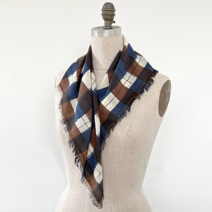 A printed plaid scarf with fringed edges draped on a beige linen dress form against a white background.