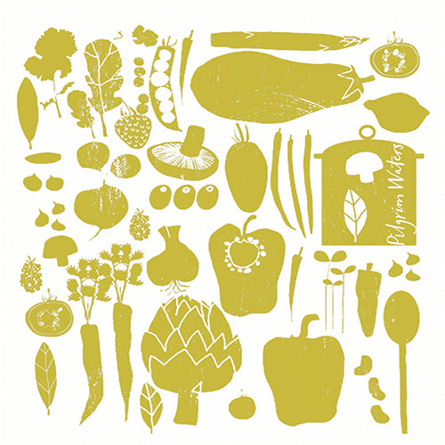 Table setting with Veggie tea towel, an olive oil bottle, a lemon, a ceramic bowl, and a green pitcher on a wooden borad.