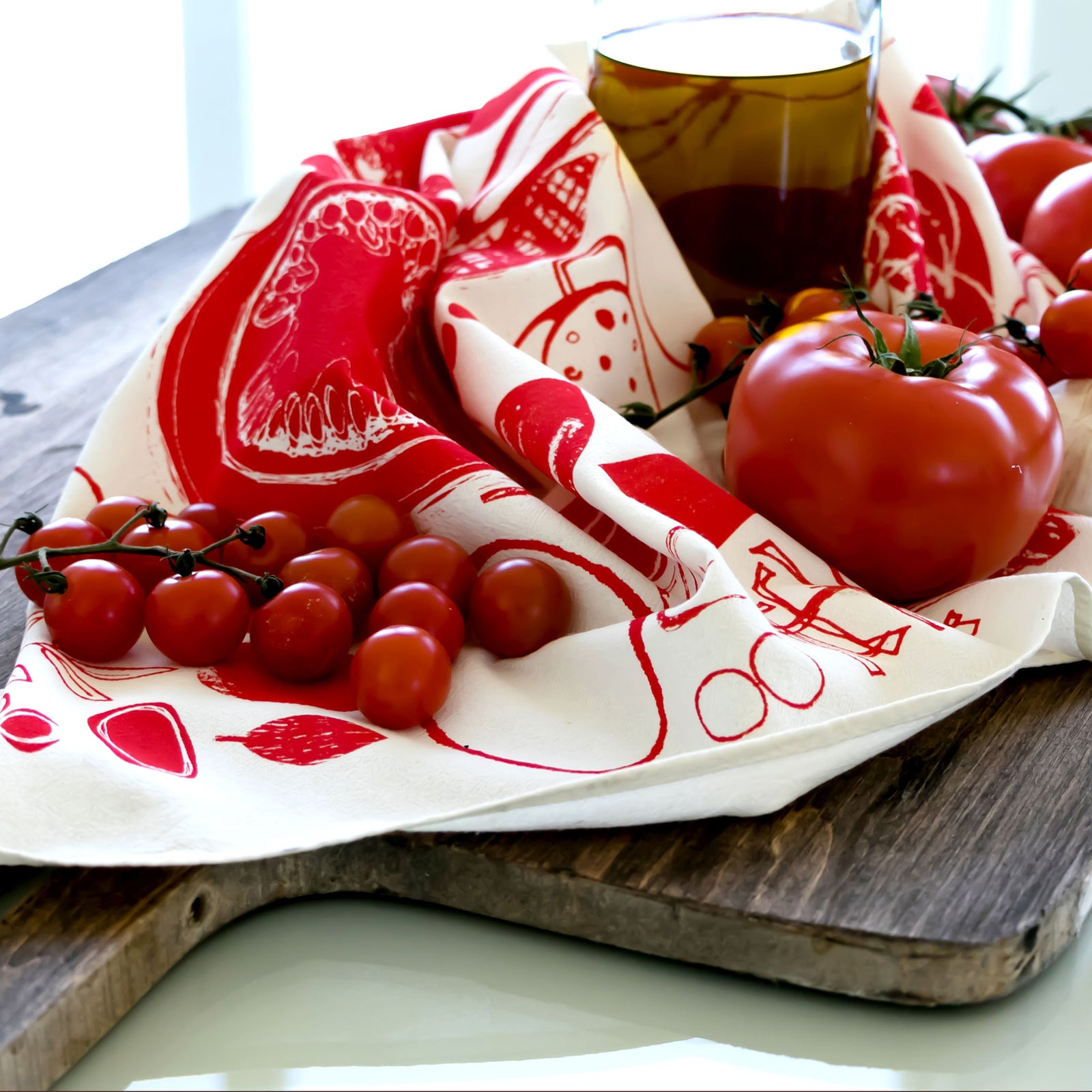 Tomatoes tea towel by PilgrimWaters, still life with breadboard, tomatoes and a bottle of olive oil. Copyright PilgrimWaters 2026.