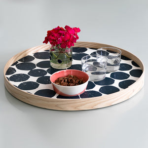 An 18-inch hand-printed round ash wood Blueberry tray styled on a modern ottoman in a brightly lit room.
