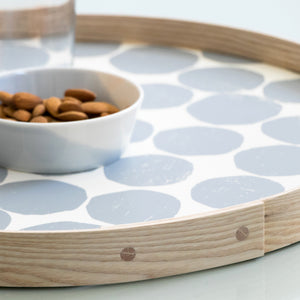 An 18-inch hand-printed round ash wood gray tray styled in close-up showing the oak pin details in a brightly lit setting.