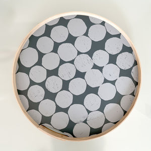 A round, Gray-on-gray dot printed tray. Hand-printed design featuring Gray PilgrimWaters dots on a dark gray background, with a natural ash wood edge. The tray is displayed head-on.